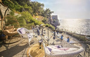 Eine Küsten-Terrasse mit Korbmöbeln, einer Seilschaukel und Blick auf das Meer.