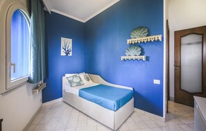Ein Schlafzimmer mit einem Bett, einem Fenster mit Vorhängen, einem Wandregal und einer Tür.