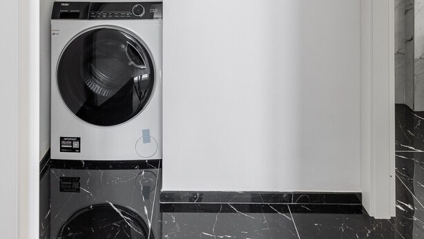 A laundry room with a front-loading washer and dryer, a water heater, and a framed abstract artwork on the wall. - La Corte Vermena by Wonderful Italy (Bologna)