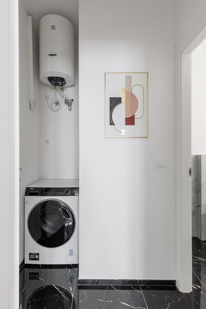 A laundry room with a front-loading washer and dryer, a water heater, and a framed abstract artwork on the wall. - La Corte Vermena by Wonderful Italy (Bologna)