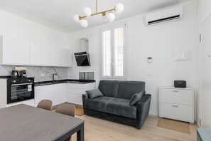 A modern kitchen with a built-in oven, a dining area with a table and chairs, a grey sofa, and a white cabinet. - La Corte Vermena by Wonderful Italy (Bologna)