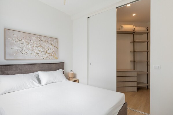 Ein Schlafzimmer mit einem Bett, einem Nachttisch, einem an der Wand befestigten Kunstwerk und einem Schrank mit Regalen.