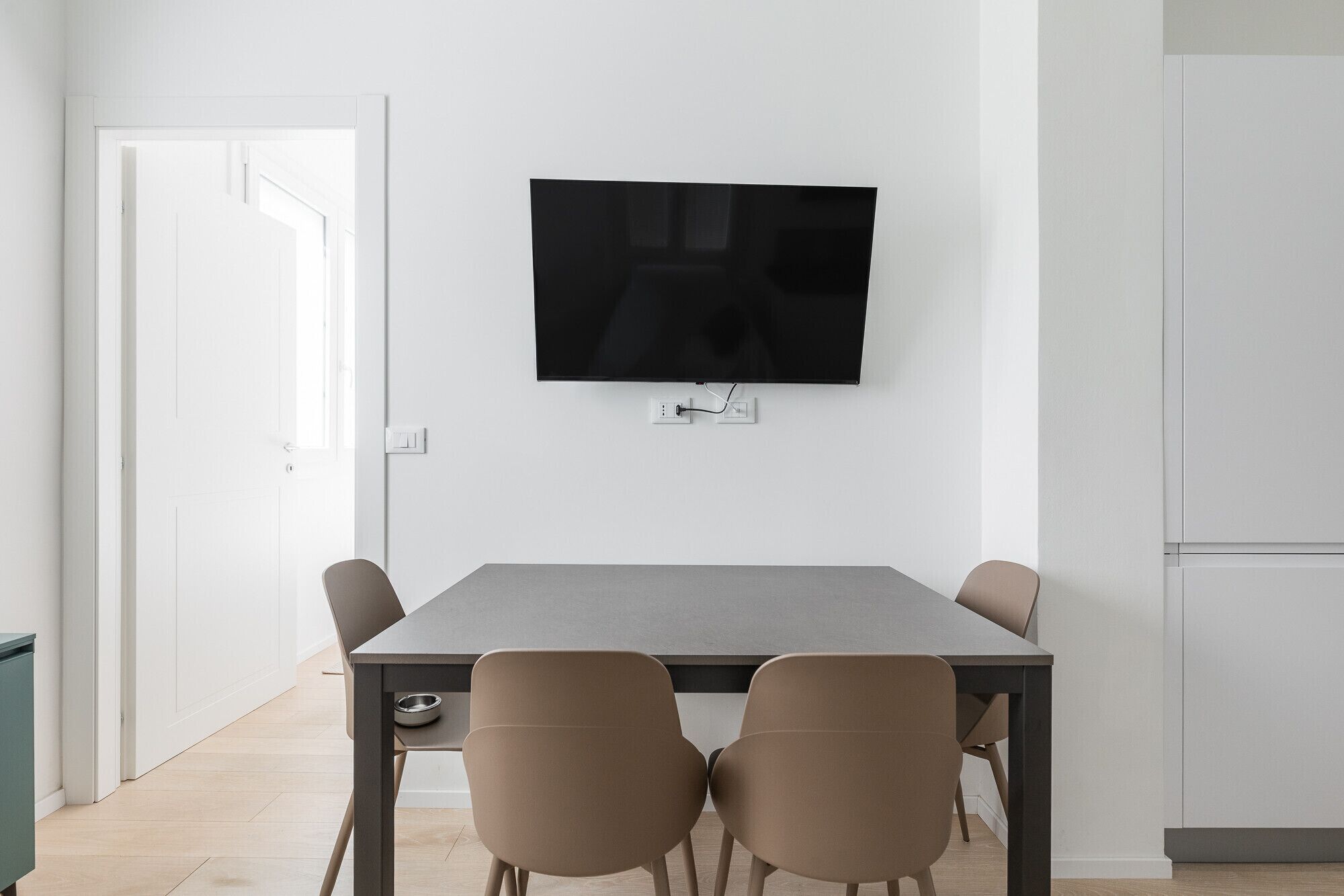 Ein stilvoller Essbereich mit Wand-Fernseher, einem rechteckigen Tisch und vier Stühlen.