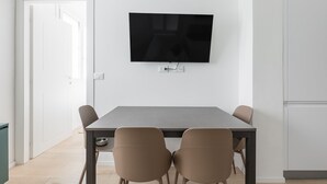 A modern dining area with a flat-screen TV mounted on the wall, a rectangular table, and four chairs. - La Corte Vermena by Wonderful Italy (Bologna)