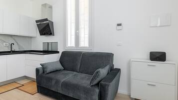 Eine moderne Küche mit weißen Schränken, einer schwarzen Dunstabzugshaube und einem grauen Sofa mit Kissen.