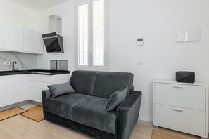 A modern kitchen with white cabinets, a black range hood, and a grey sofa with cushions.