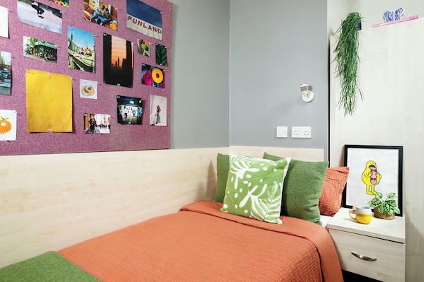 A bedroom with a bed, pillows, a wall with photos, a plant, and a framed picture.