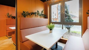 A modern interior with a white table, cushioned seating, and a window with a view of buildings and trees. - Student Only Newarke Point (Leicester)
