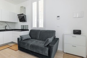 Eine moderne Küche mit weißen Schränken, einem grauen Sofa und einem kleinen, weißen Schrank mit einem schwarzen Lautsprecher.