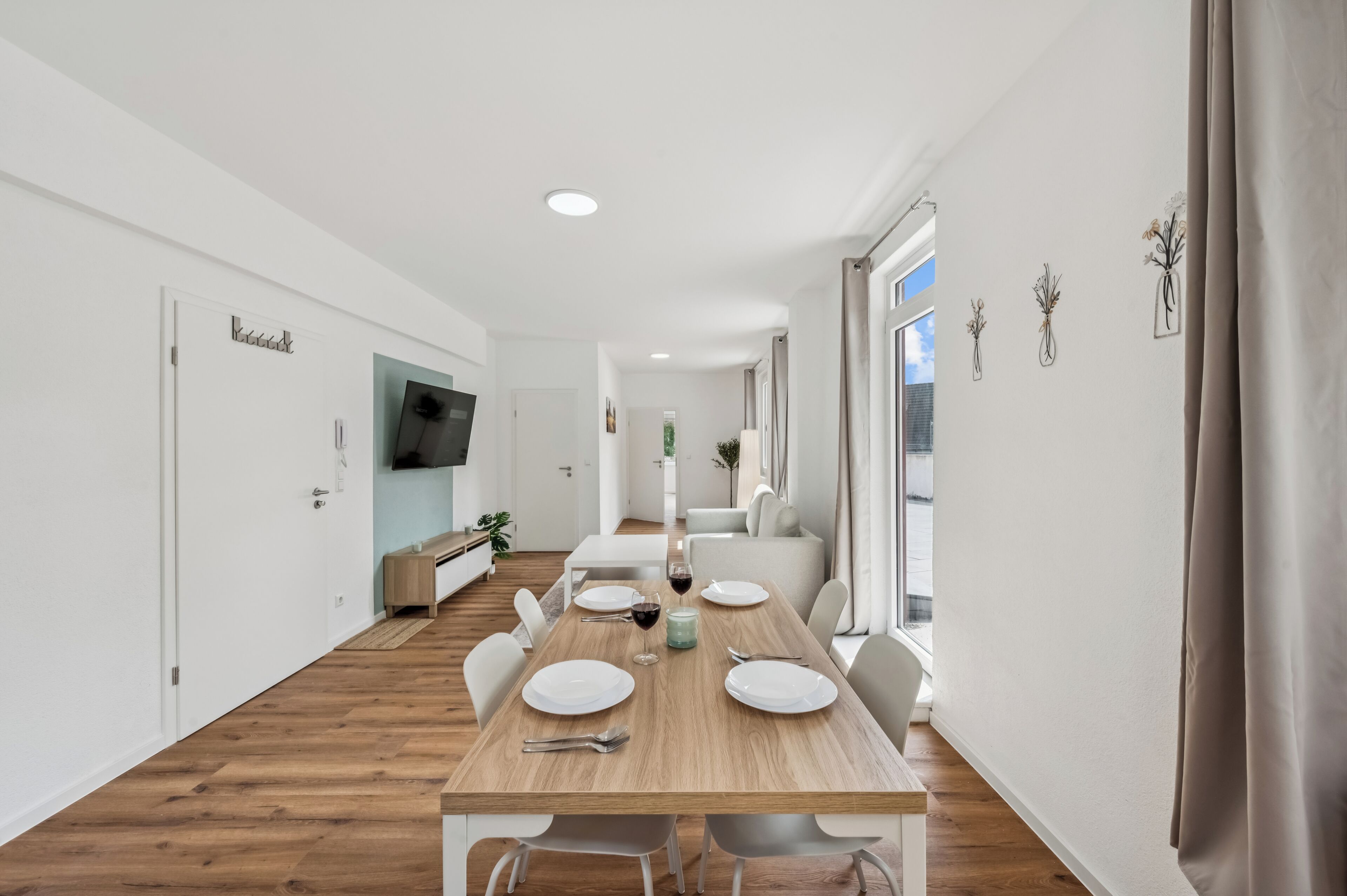 A modern dining area with a wooden table set for four, white chairs, and a television mounted on the wall.