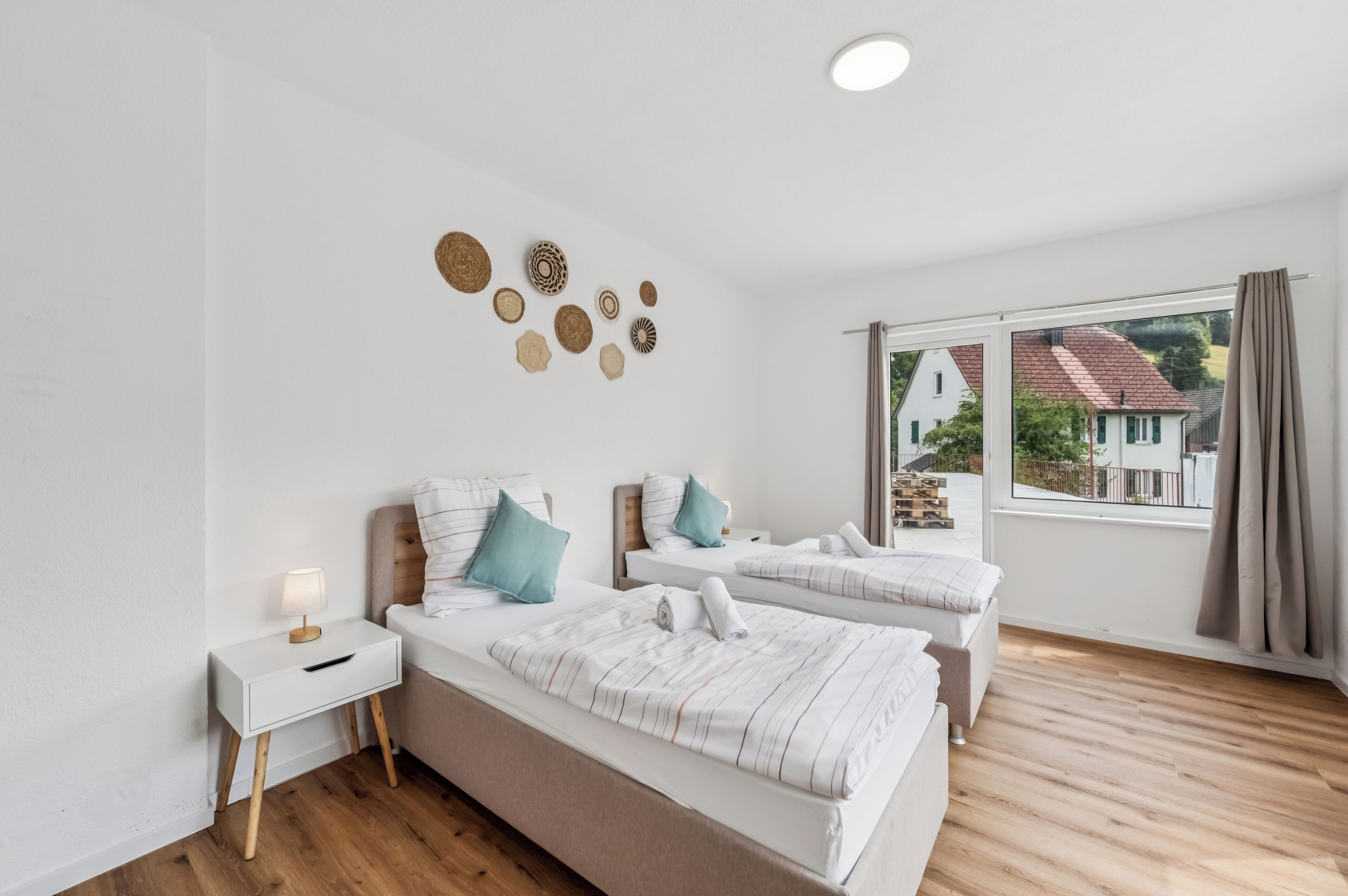 A hotel room with two beds, a bedside table, a lamp, a view of the outside, and a wall with decorative items.