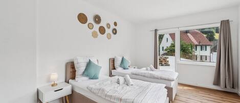 A hotel room with two beds, a bedside table, a lamp, a view of the outside, and a wall with decorative items.