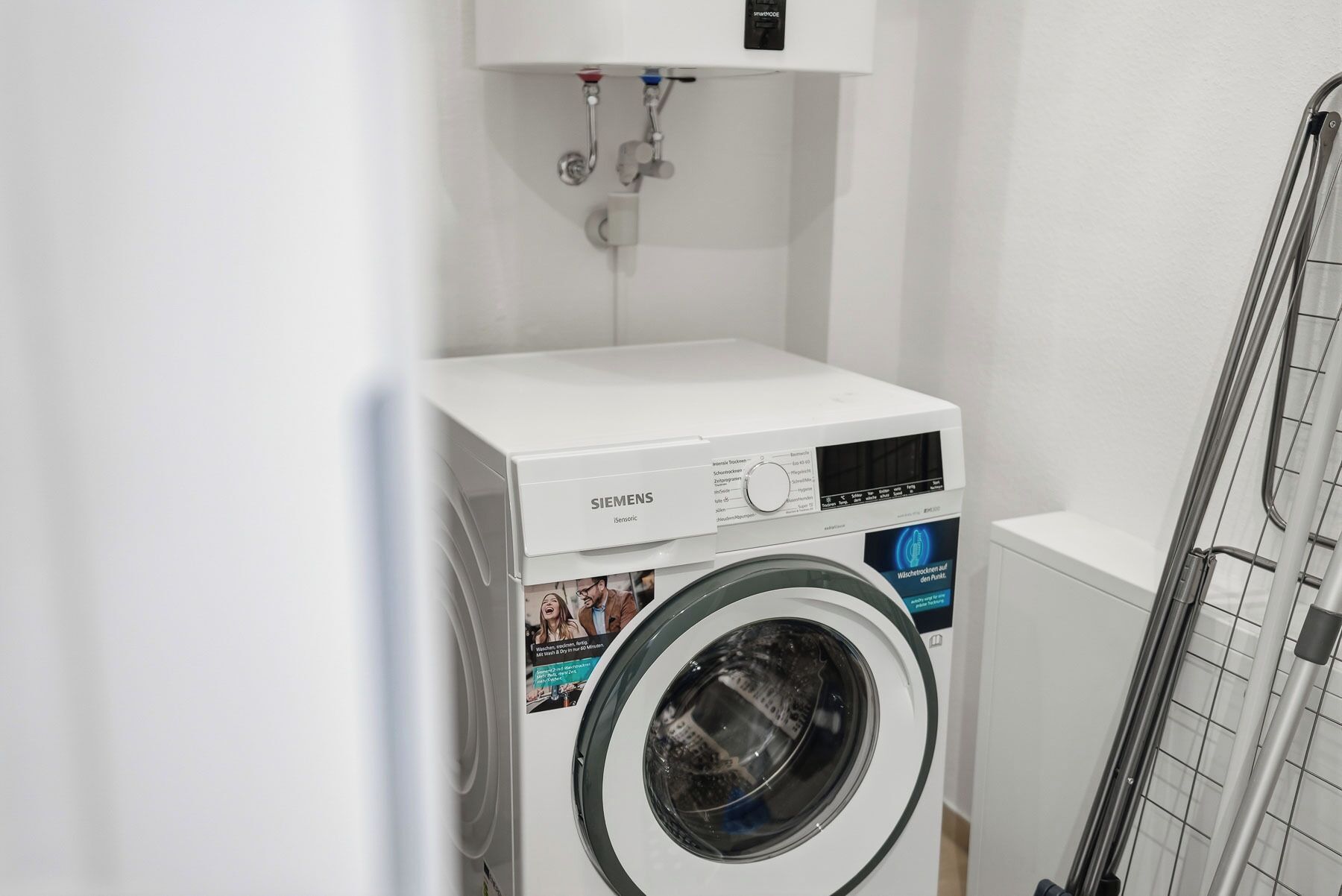 Eine weiße Siemens Waschmaschine in einem Hauswirtschaftsraum mit einem Metallgestell und einer weißen Wand.