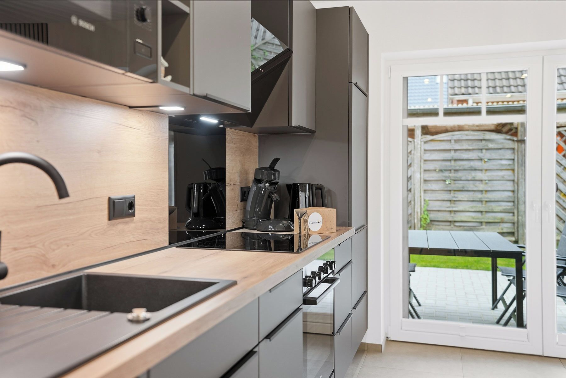 A modern kitchen with a built-in stove, coffee maker, and storage cabinets.