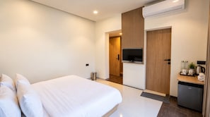Una habitación de hotel con una cama, televisor, minibar y puerta que da a un baño.