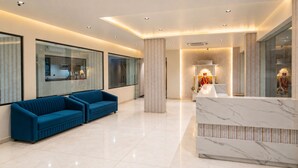 Un moderno vestíbulo con un sofá azul, mostrador de recepción de mármol y una pared decorativa.