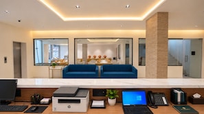 Una moderna zona de recepción con mostrador de mármol, computadoras HP y Dell, una impresora y un sofá azul.