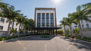 A modern building with 'The Eco Satva' signage, surrounded by palm trees and a well-maintained garden.
