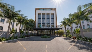 Un edificio moderno con el letrero 'The Eco Satva', rodeado de palmeras y un jardín bien cuidado.