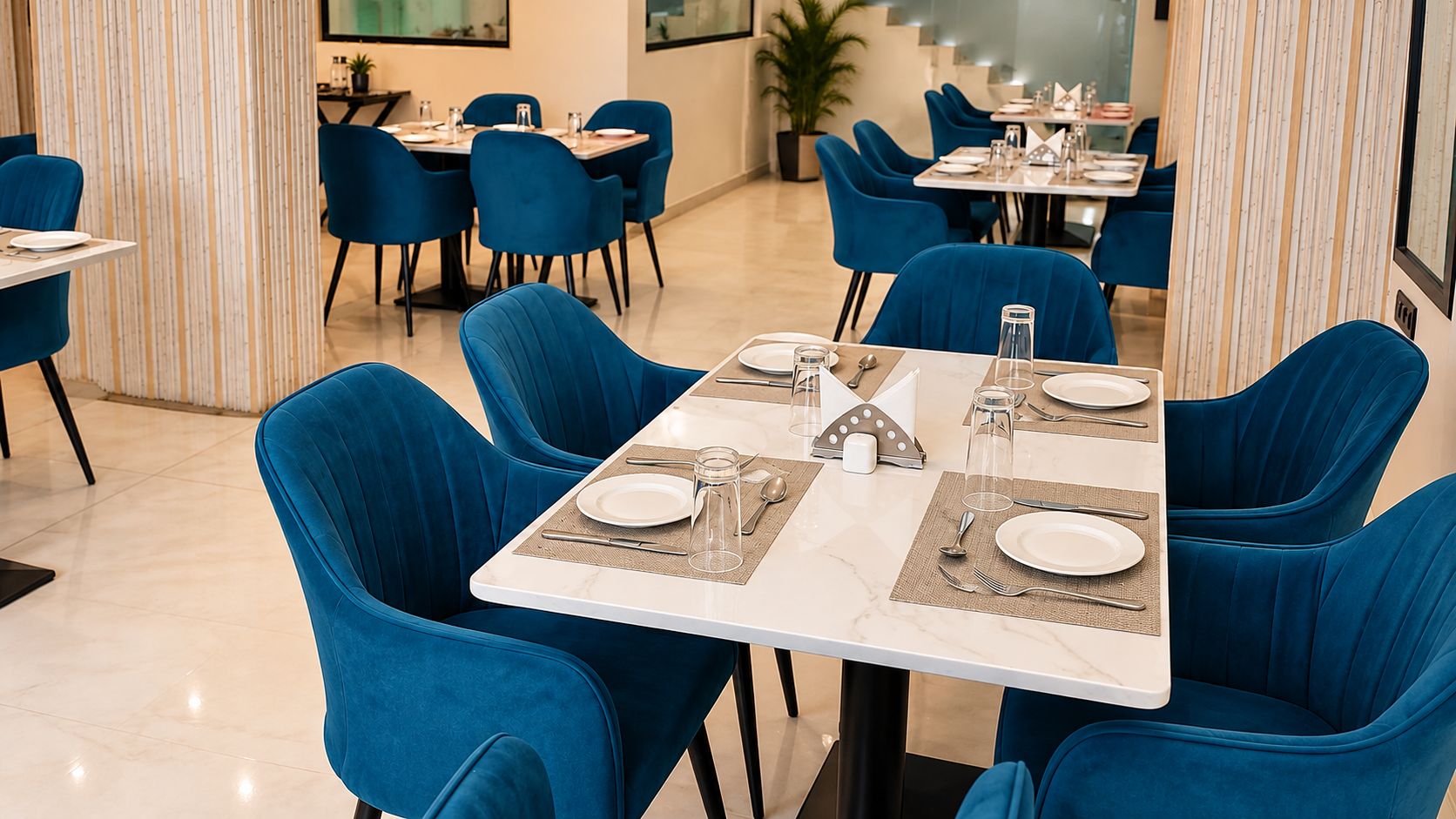 Un comedor con sillas azules y mesas blancas, equipado con cubiertos y vasos.