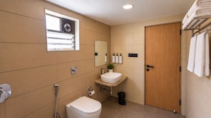 A modern bathroom with a toilet, sink, and shower. There is a window with blinds, a towel rack, and a door.