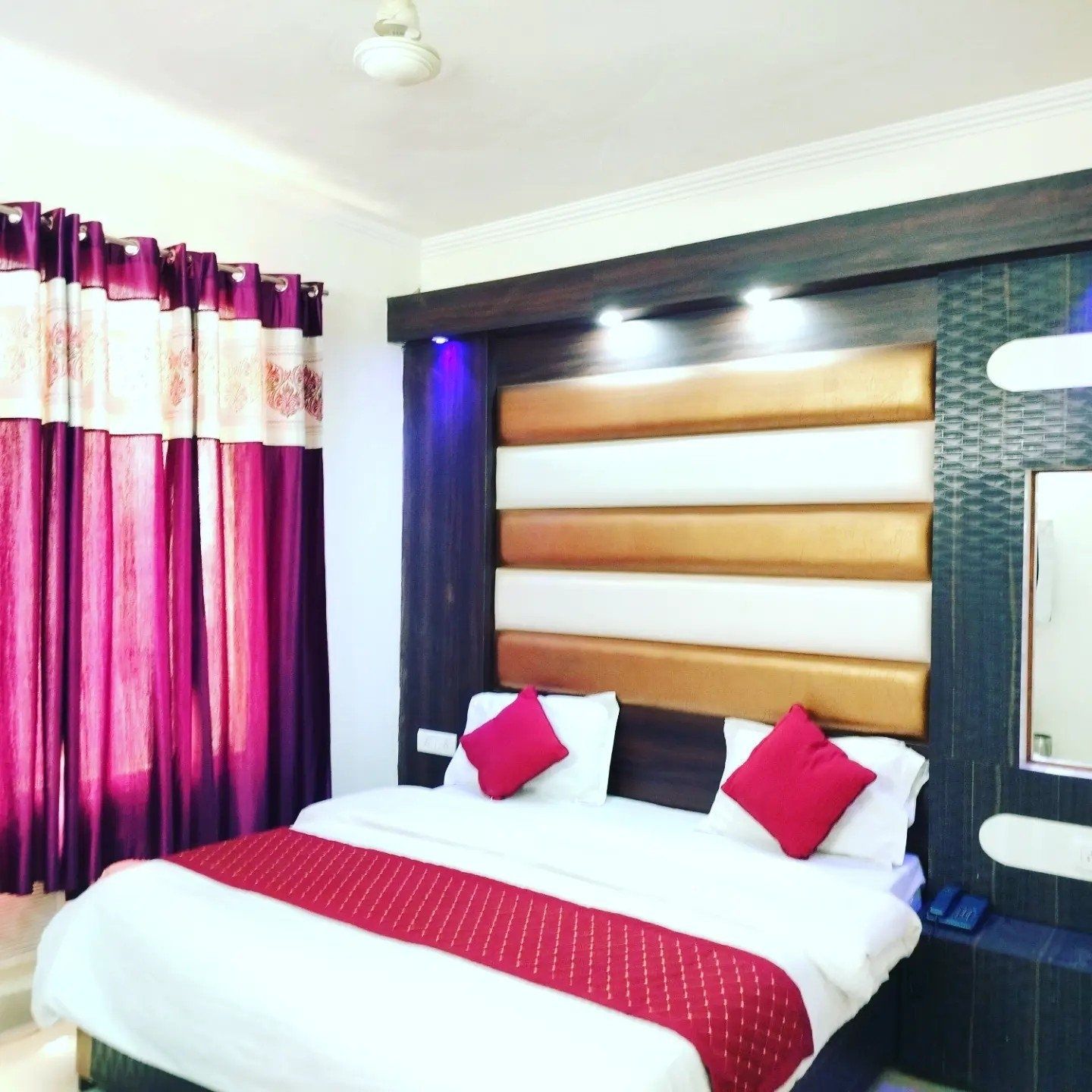Quarto de hotel com cama, cortinas, cabeceira e mesa de cabeceira.