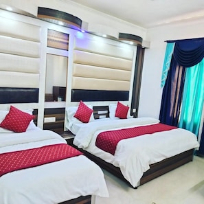 Habitación de hotel con tres camas, cada una con ropa blanca y almohadas rojas. La habitación tiene un diseño moderno, un cabecero oscuro y una pared de color claro.