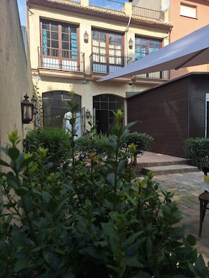 A courtyard with a building featuring large windows and a covered area. - Lotel Casa Noble La Solana (València)