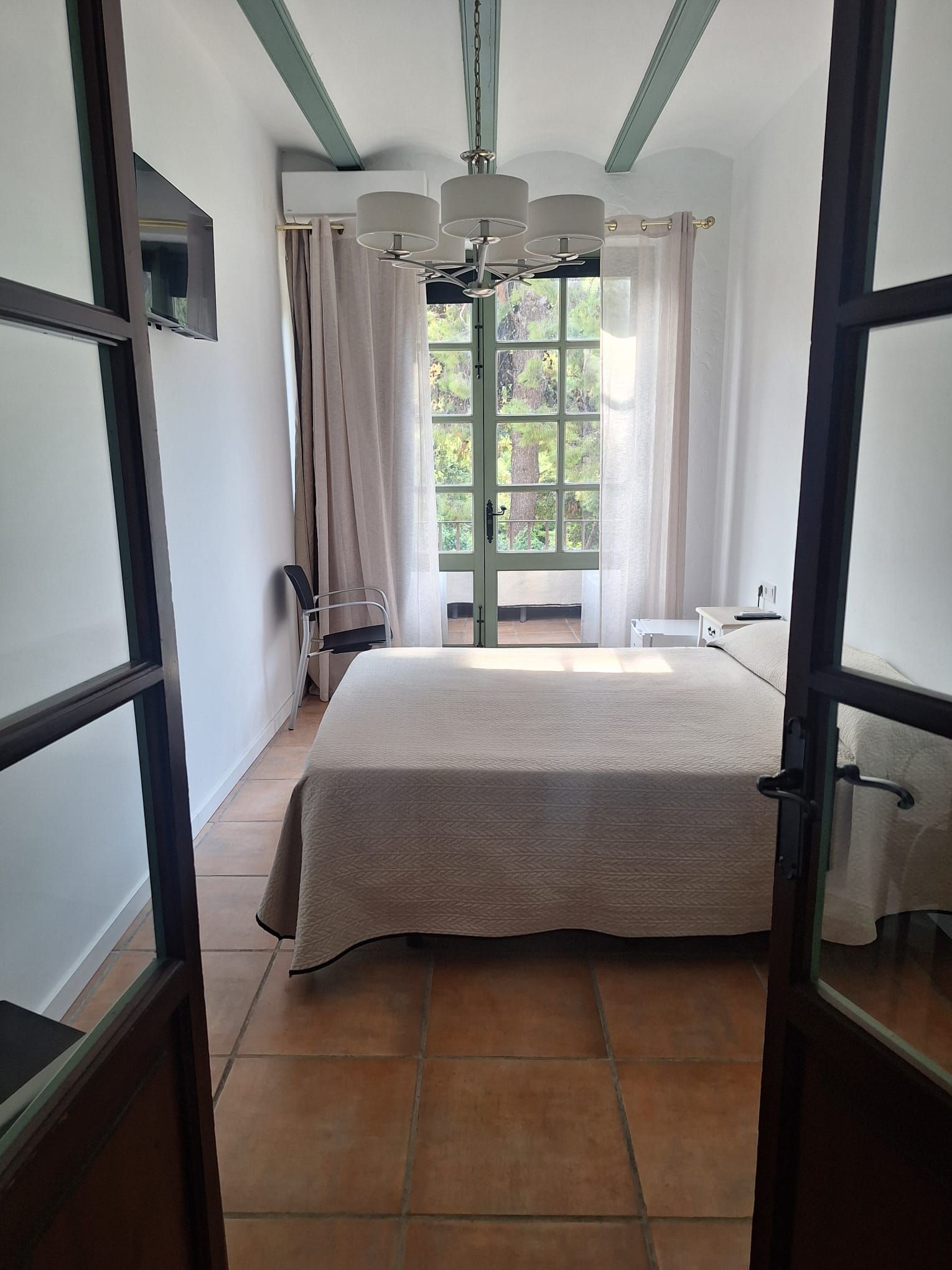 A bedroom with a bed, a chair, a table, and a window with curtains.