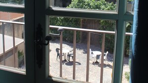 Vista a través de una ventana con barandilla de metal, un patio con sillas y una mesa, y follaje al exterior.
