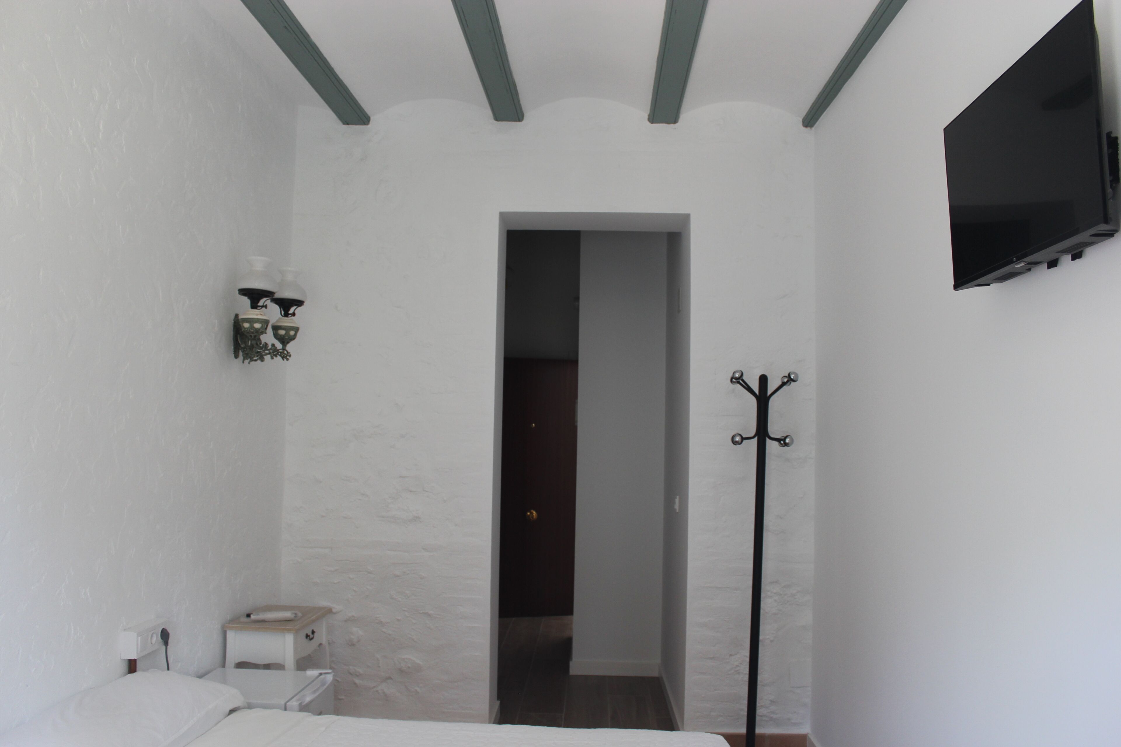 A bedroom with a bed, a bedside table, a TV mounted on the wall, and a coat rack.