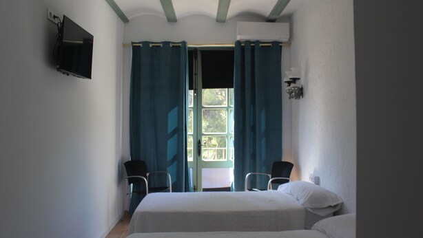 Una habitación con una cama, dos sillas, un televisor y un ventanal con cortinas.