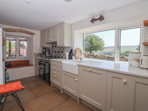 A kitchen with a stove, oven, and sink, a window with a view of the countryside, and a wooden bench. - Lyndhurst (Leyburn)