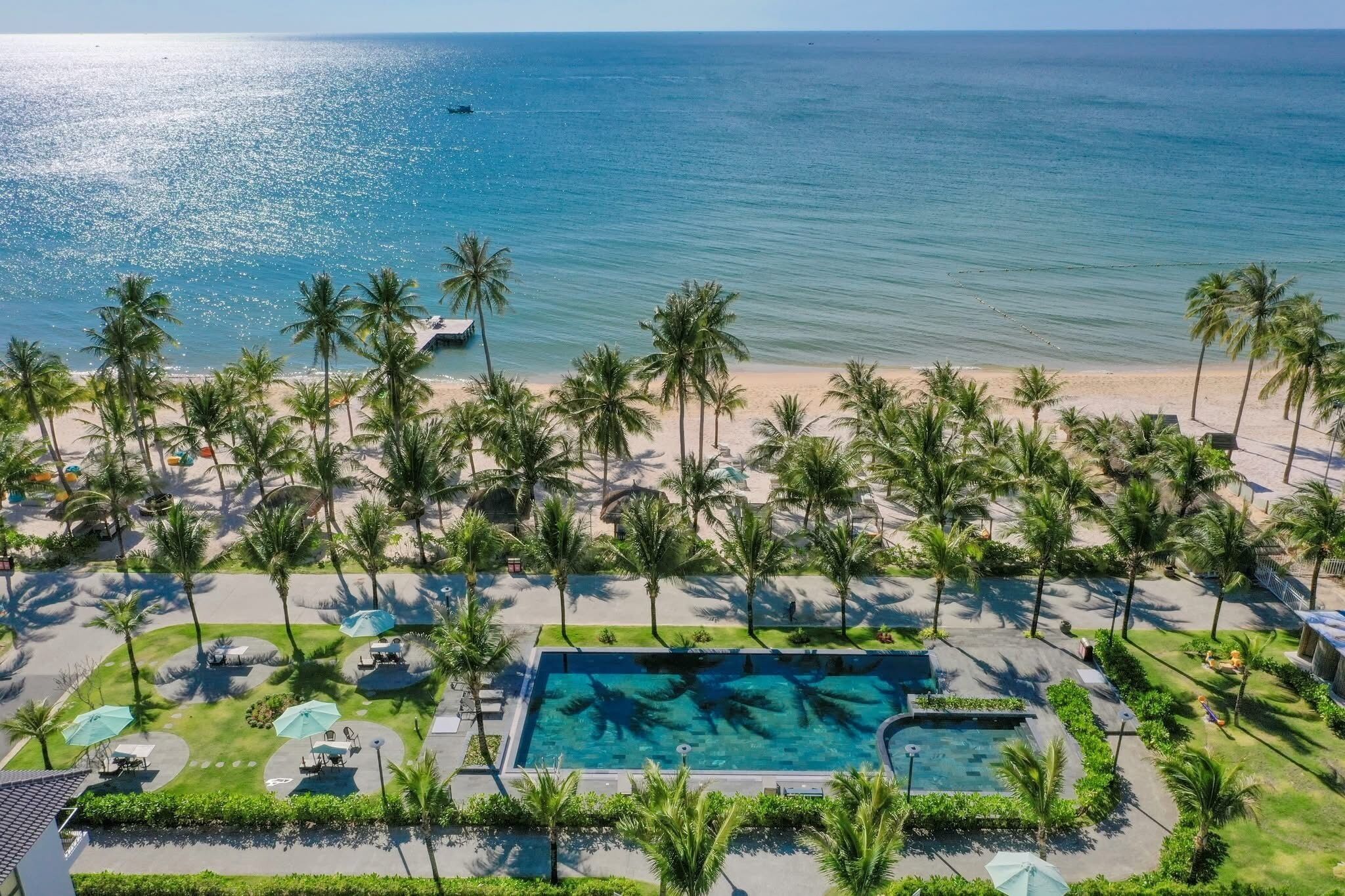 A resort with a swimming pool, palm trees, and a beach.