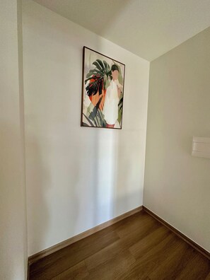 Ein Flur mit Holzboden, weißer Wand und einem Bilderrahmen mit einem tropischen Motiv.