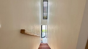 Eine schmale Treppe mit Holzwegen führt zu einer Zwischenebene mit einem Fenster.