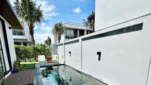 Ein moderner Außenpool mit transparentem Glasboden, umgeben von einer weißen Wand und einer Holzterrasse.