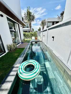 Un área de piscina moderna con una superficie de agua cristalina, rodeada de paredes blancas y una terraza de madera.
