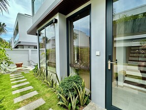 Una casa moderna con puerta de vidrio, un camino pavimentado y un pequeño jardín con plantas.