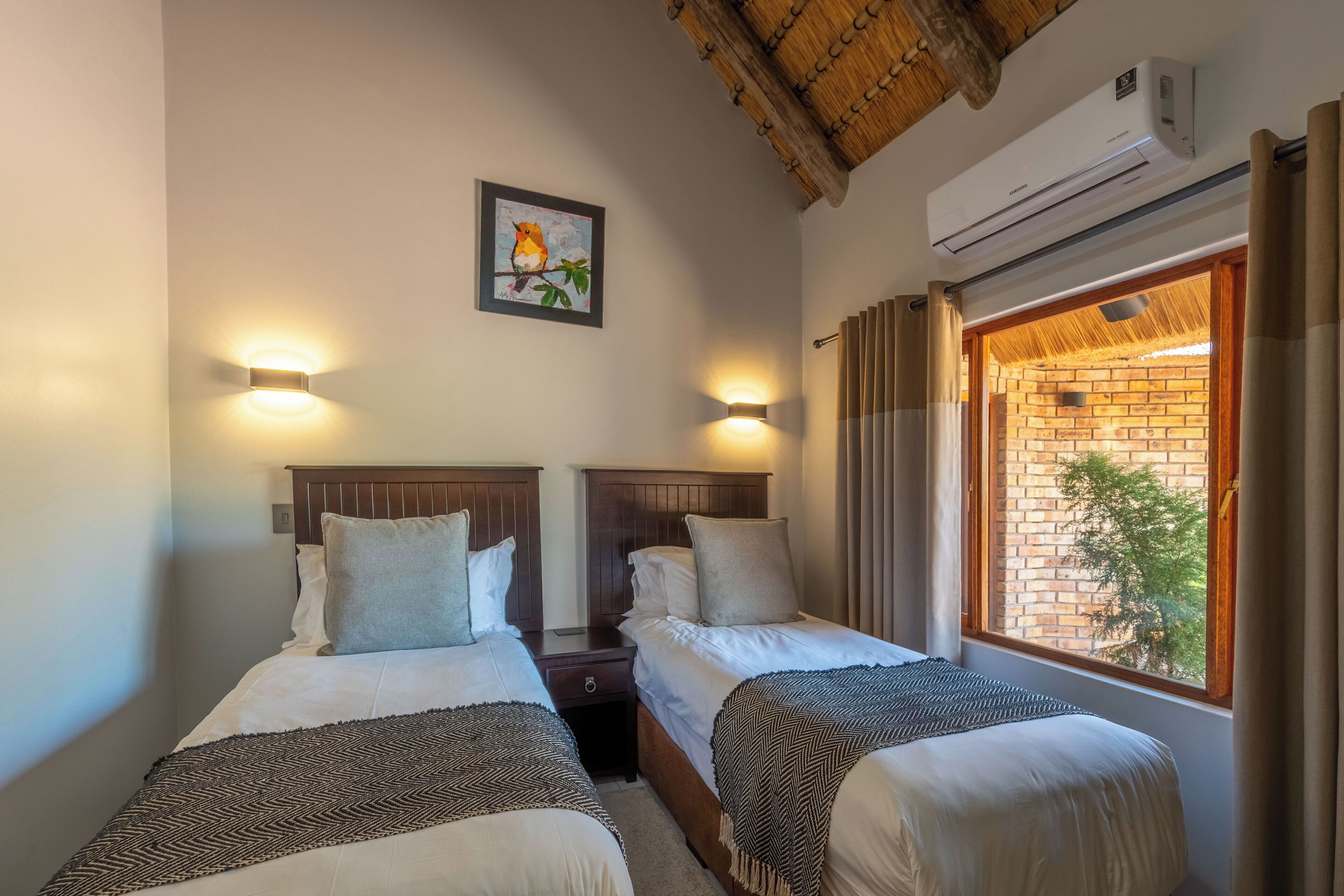 A hotel room with two beds, a framed picture on the wall, and an air conditioning unit above the window.