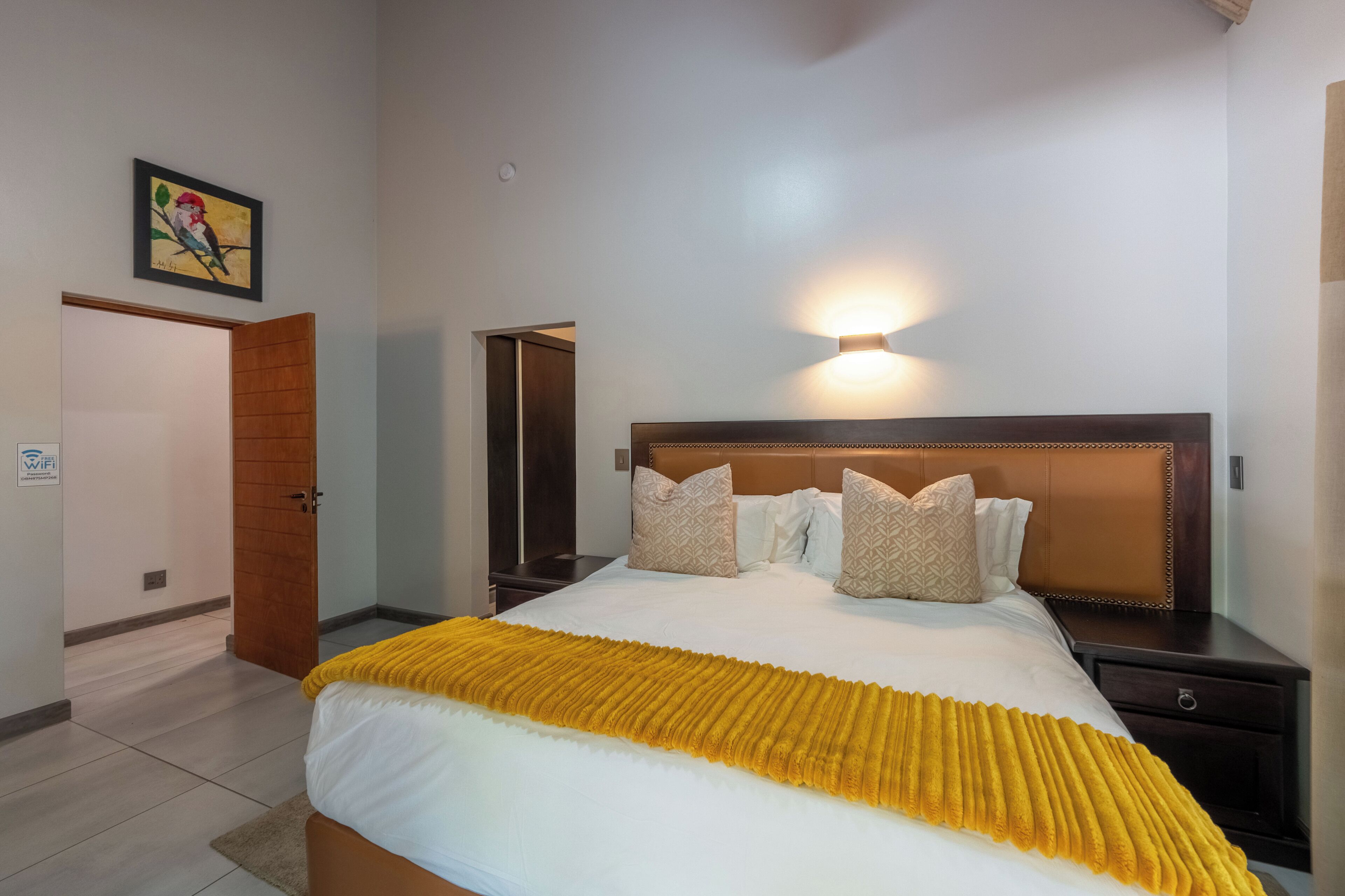 A hotel room with a bed, a nightstand, a wall-mounted lamp, a door, and a painting on the wall.