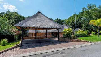 A thatched-roof structure with a brick base, surrounded by greenery and a paved walkway.