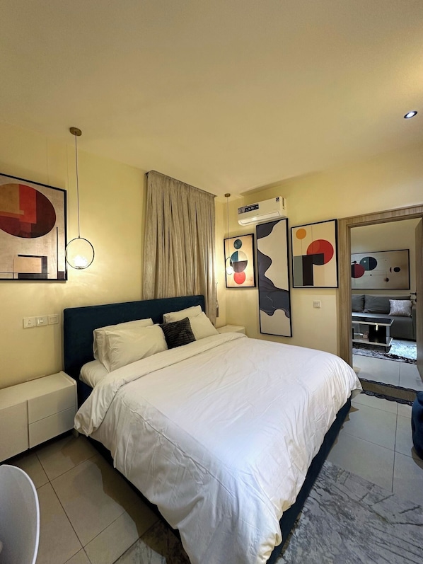 Une chambre d’hôtel comprenant un lit, une table de chevet, une chaise, un climatiseur fixé au mur et des œuvres d’art abstrait accrochées aux murs.