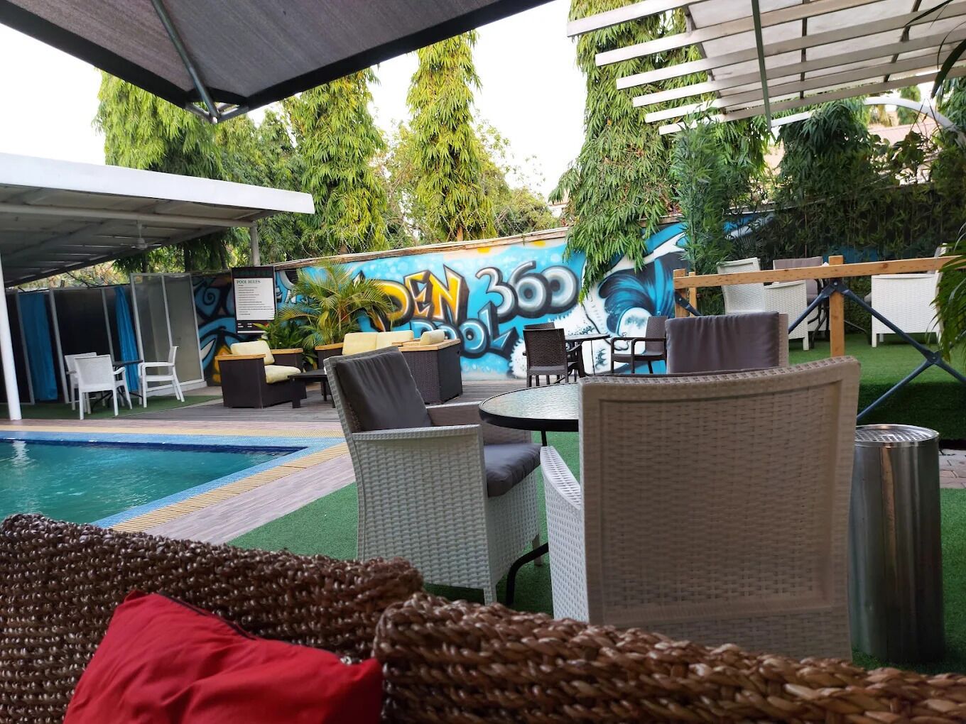 An outdoor seating area with wicker furniture, a pool, and a mural in the background.