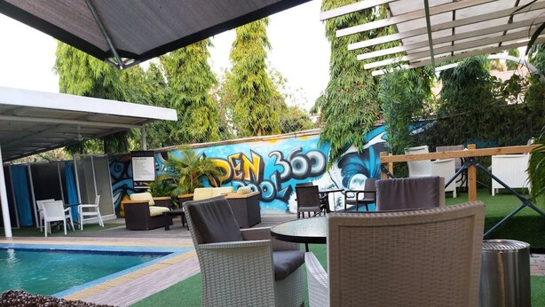 An outdoor seating area with wicker furniture, a pool, and a mural in the background. - Aden 360 By Intra  (Abuja)