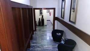 A hallway with a marble floor, wooden doors, a black chair, and a framed picture on the wall. - Aden 360 By Intra  (Abuja)