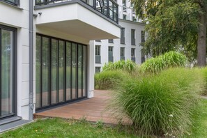 A modern building with large glass windows, a wooden deck, and a well-maintained garden with tall grass. - Apartment Seeschwalbe: Fireplace, Pool, Terrace, Wi-Fi – Exclusive Baltic Sea Holiday in Binz (Binz)