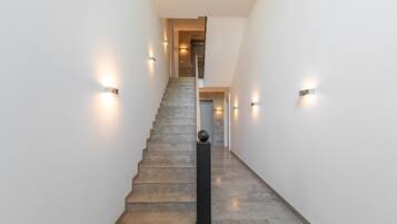 Un escalier avec une rampe, des murs équipés de luminaires et une porte en haut.