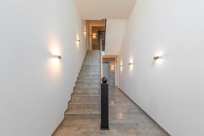 Un escalier avec une rampe, des murs équipés de luminaires et une porte en haut.