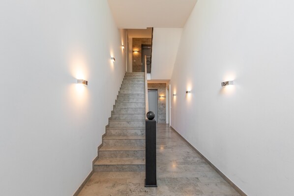 A staircase with a handrail, walls with light fixtures, and a door at the top.